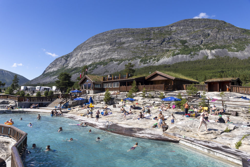 Uteareal med badebasseng og folk som bader og koser seg i sola på svaberget.